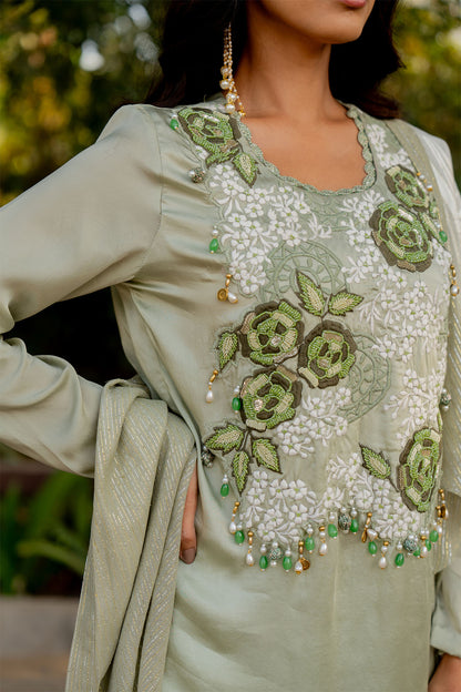 Box pleat pants and an embroidered vest are paired with a long cape