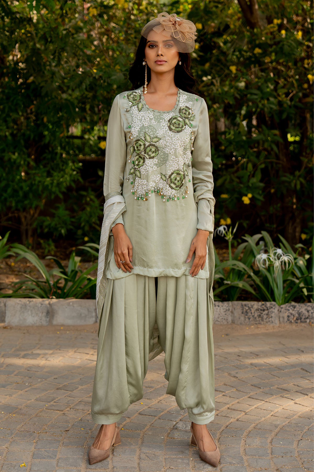 Box pleat pants and an embroidered vest are paired with a long cape