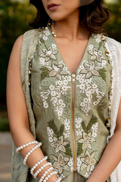 Box pleat pants and an embroidered vest are paired with a long cape