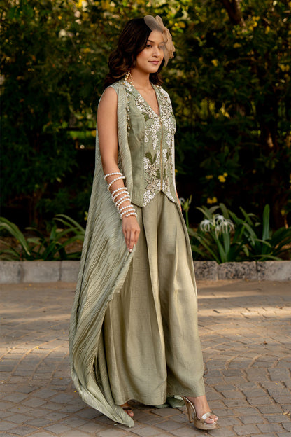 Box pleat pants and an embroidered vest are paired with a long cape